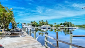 A wooden pier with lounge chairs and umbrellas, leading to a marina with boats and palm trees. - ALL-NEW Waterfront Room, Heated Pool, Tiki Bar/Grill (Sarasota)