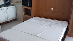 Un dormitorio con estructura de cama de madera, una mesita de noche pequeña de madera, un microondas y un armario blanco.