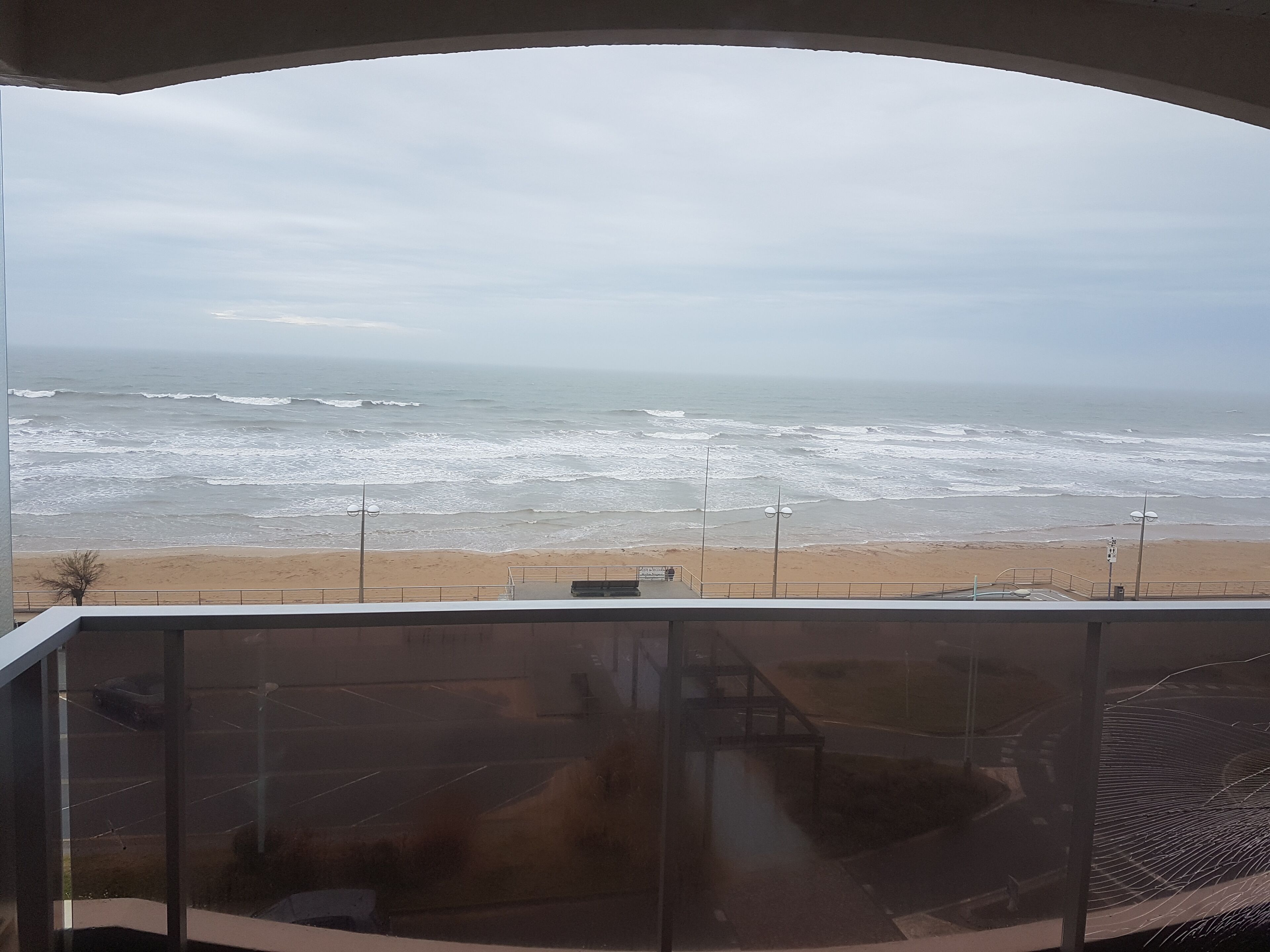 A view of the beach from a balcony with a railing, a street lamp, and a clear sky.