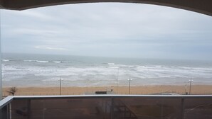 Vista de la playa desde un balcón con barandilla, un farol y cielo despejado.