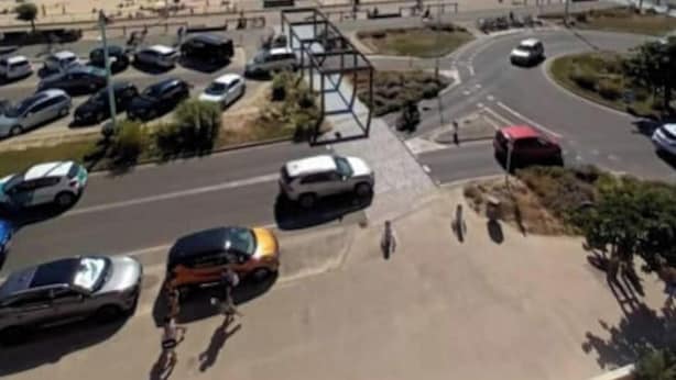 Un estacionamiento con autos, cielo despejado y una playa al fondo.