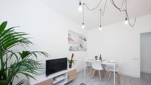 A modern living room with a TV, dining table, chairs, and a plant.
