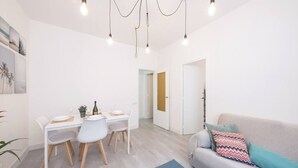 A modern living room with a dining area, white walls, and a grey sofa with colorful cushions.