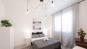 A modern bedroom with a large bed, bedside tables, a dresser, and a potted plant.