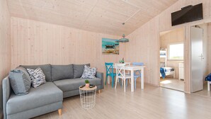 A modern living room with a grey sofa, a small round table with a plant, and a dining area with white chairs and a blue table. - Stunning home in Darlowo with WiFi (Darlowo)