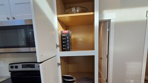 Una cocina con microondas, estufa y alacena abierta que muestra utensilios de cocina y un escurreplatos.