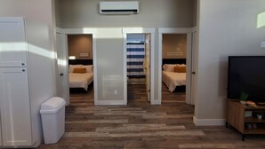 Habitación de hotel compacta con kitchenette, cama con cortina a rayas y un televisor pequeño sobre un atril de madera.