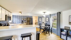 A modern kitchen with a central island, bar stools, and a dining area with chairs. - Camp-Style Cabin Near Pigeon Forge: Fire Pit, Deck (Sevierville)
