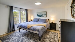 A bedroom with a bed, bedside tables, a dresser, a window with curtains, a painting on the wall, and a rug. - Camp-Style Cabin Near Pigeon Forge: Fire Pit, Deck (Sevierville)