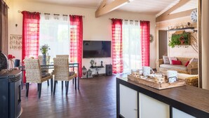 Un salon chaleureux avec un téléviseur, des meubles en osier, une table à manger et des rideaux rouges.