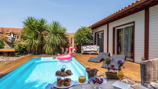 Un petit-déjeuner servi au bord de la piscine, avec des croissants, des fruits et des boissons, entouré de chaises longues et agrémenté d’un flotteur en forme de flamant rose.
