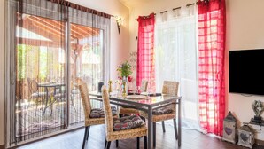Un coin repas avec des chaises en osier, une table en verre et des rideaux rouges.