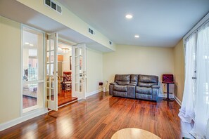 A spacious living room with hardwood flooring, a leather sofa, and a dining area visible through an open door.