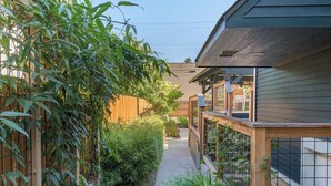 Un sendero estrecho bordeado de bambú y otra vegetación, que conduce a una terraza de madera con barandilla.