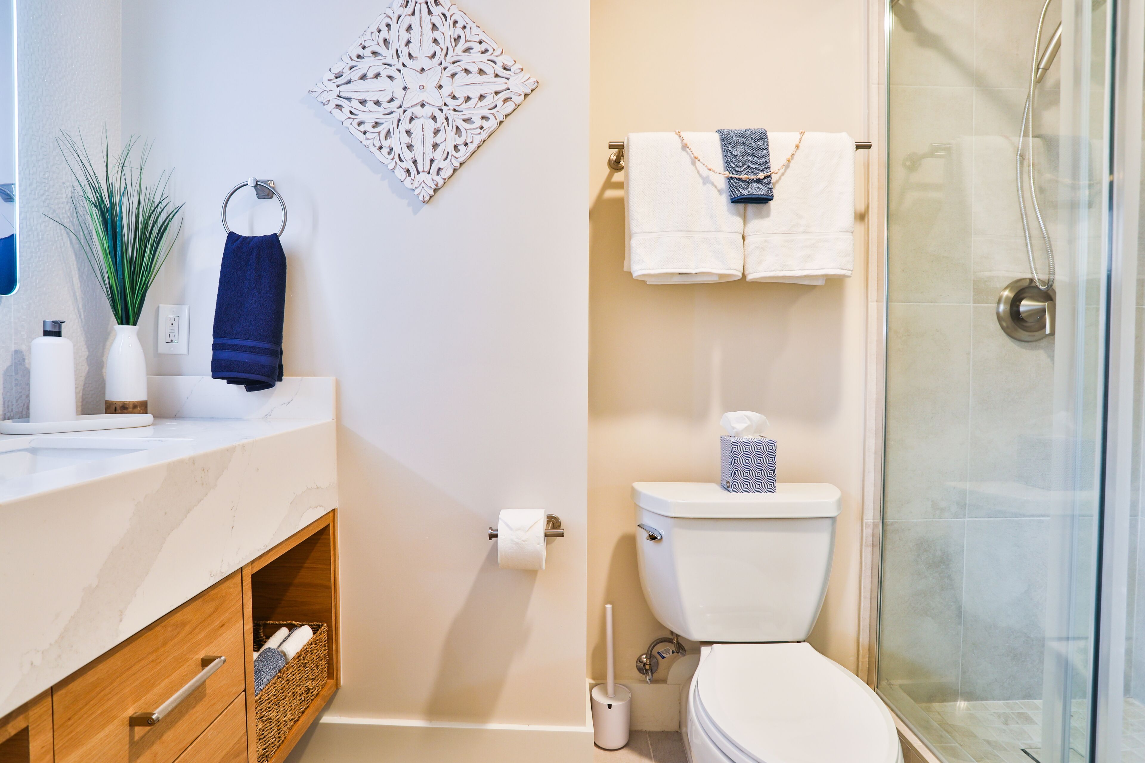 A bathroom with a toilet, a glass shower enclosure, a sink with a marble countertop, and a decorative wall piece.