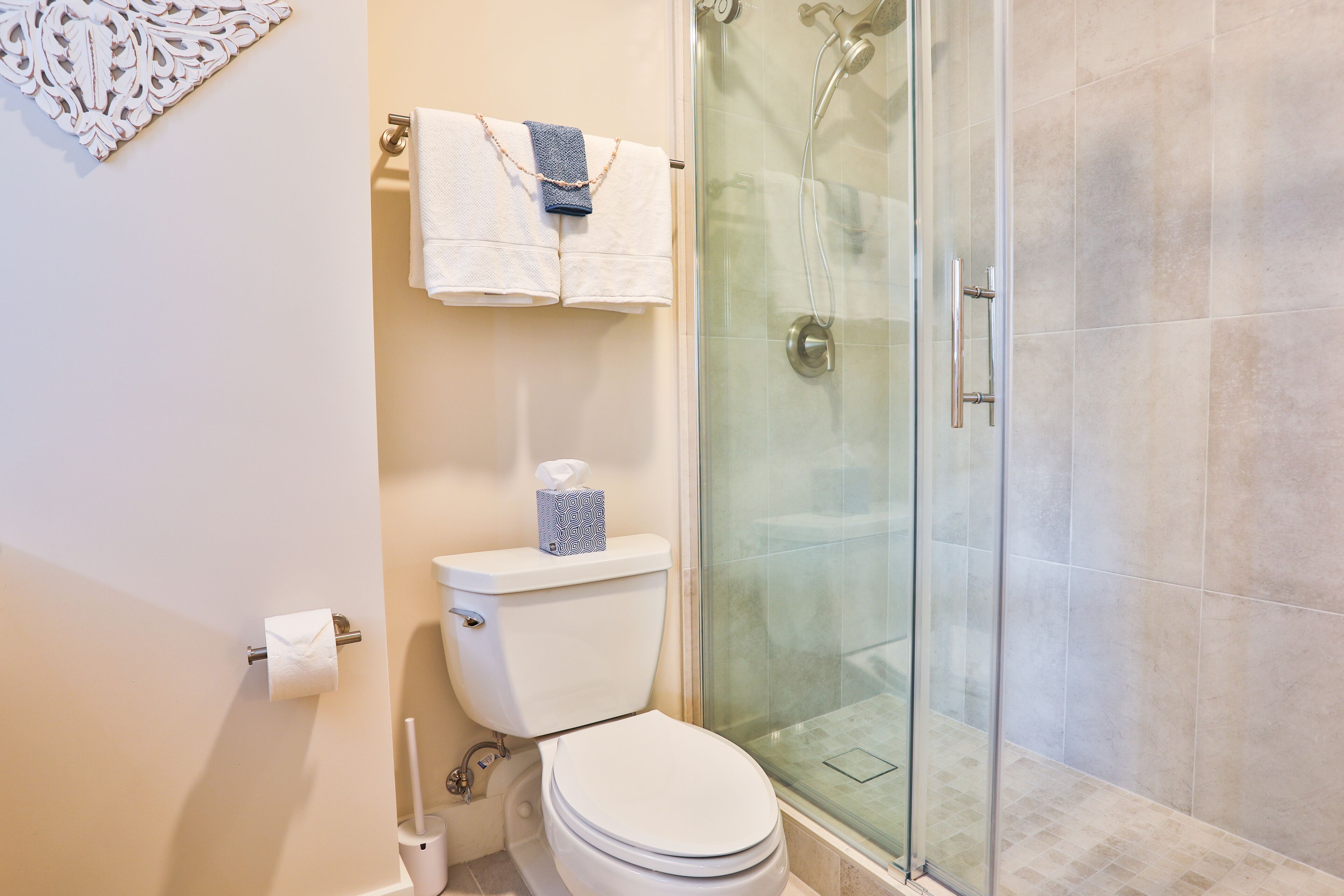 A bathroom with a toilet, a glass shower enclosure, and a towel rack with two towels.