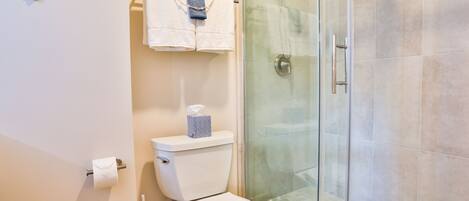 A bathroom with a toilet, a glass shower enclosure, and a towel rack with two towels.