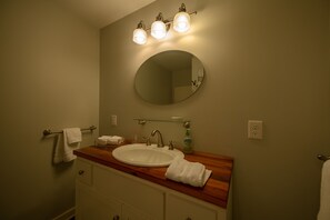 Ein Badezimmer mit rundem Spiegel, einem Holzanrichte, einem weißen Waschbecken und einem Handtuchhalter.