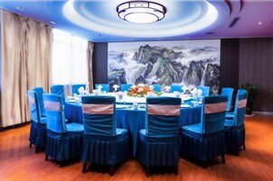 Un salón de conferencias con una mesa redonda, sillas azules y un cuadro de montañas en la pared.