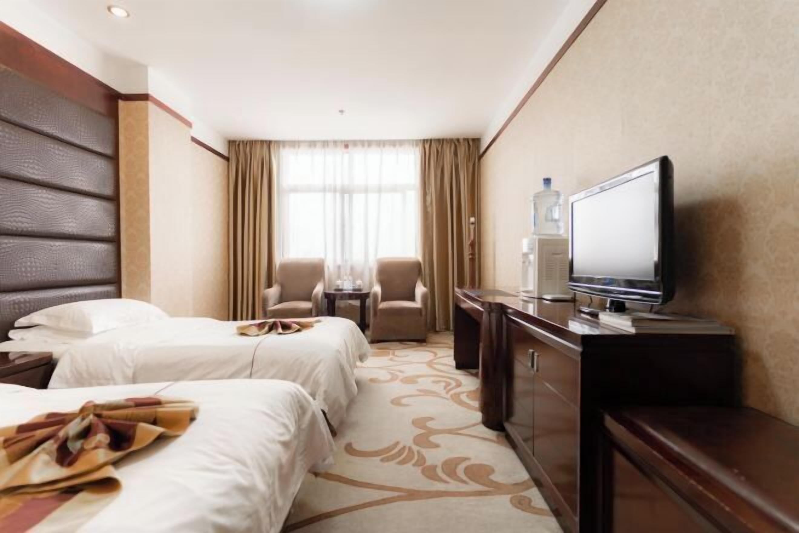 A hotel room with two beds, a television, a desk, and a chair.