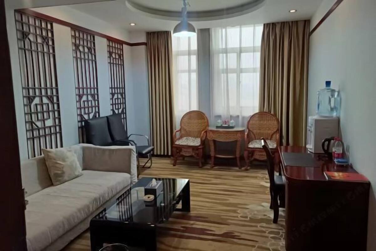Ein Hotelzimmer mit einer Couch, zwei Korbstühlen, einem kleinen Tisch, einem Couchtisch, einem Wasserspender und einem Fernseher.
