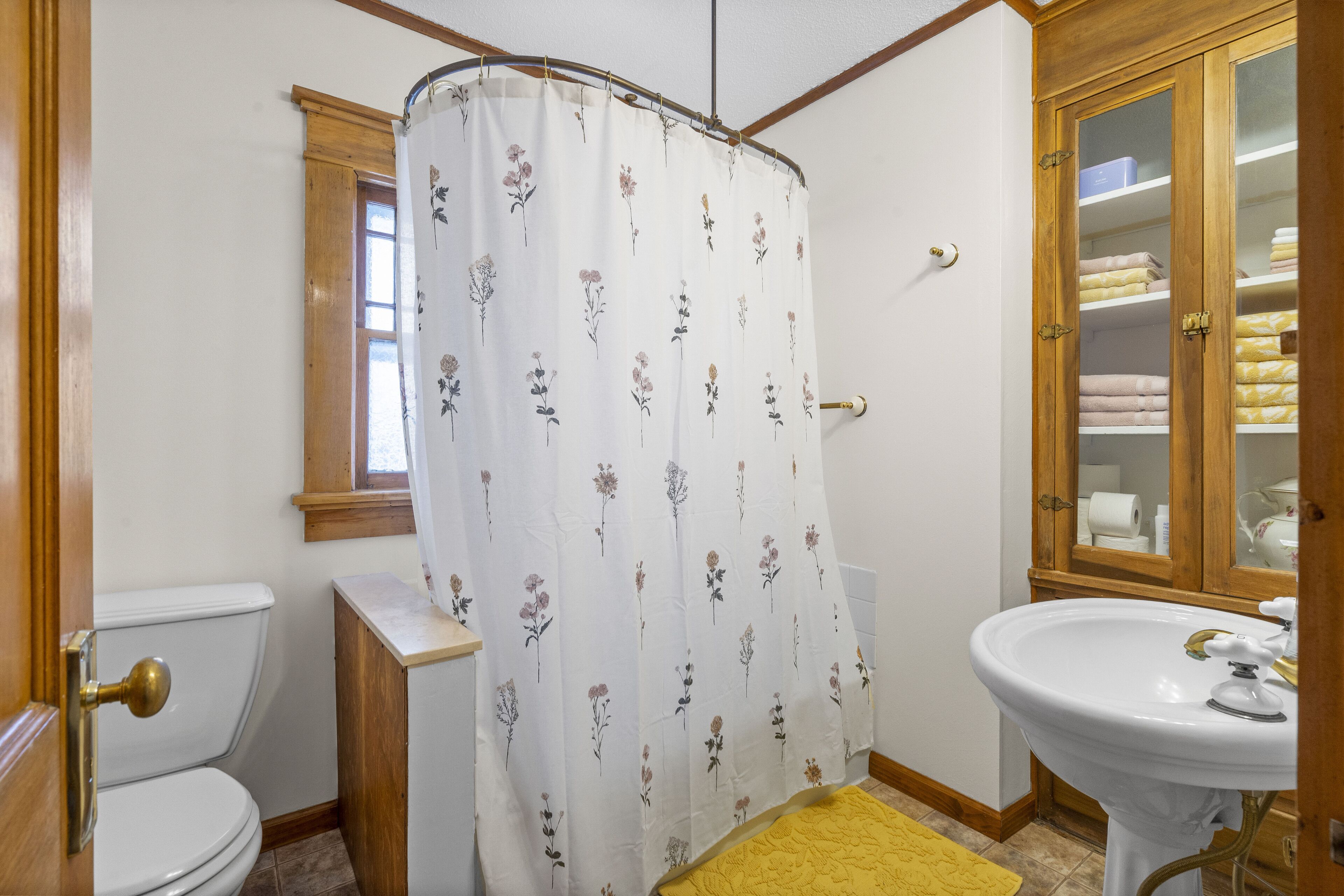 Et badeværelse med toilet, vask, bruseforhæng og et træskab.
