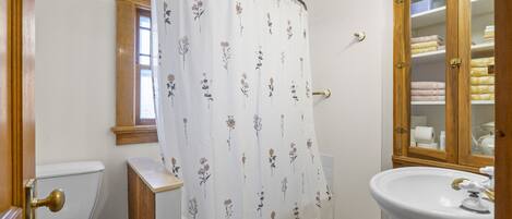 Et badeværelse med toilet, vask, bruseforhæng og et træskab.