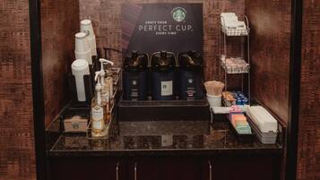 Una estación de café con productos Starbucks, incluyendo tazas, una máquina de café y un cartel que invita a los huéspedes a preparar su taza perfecta.