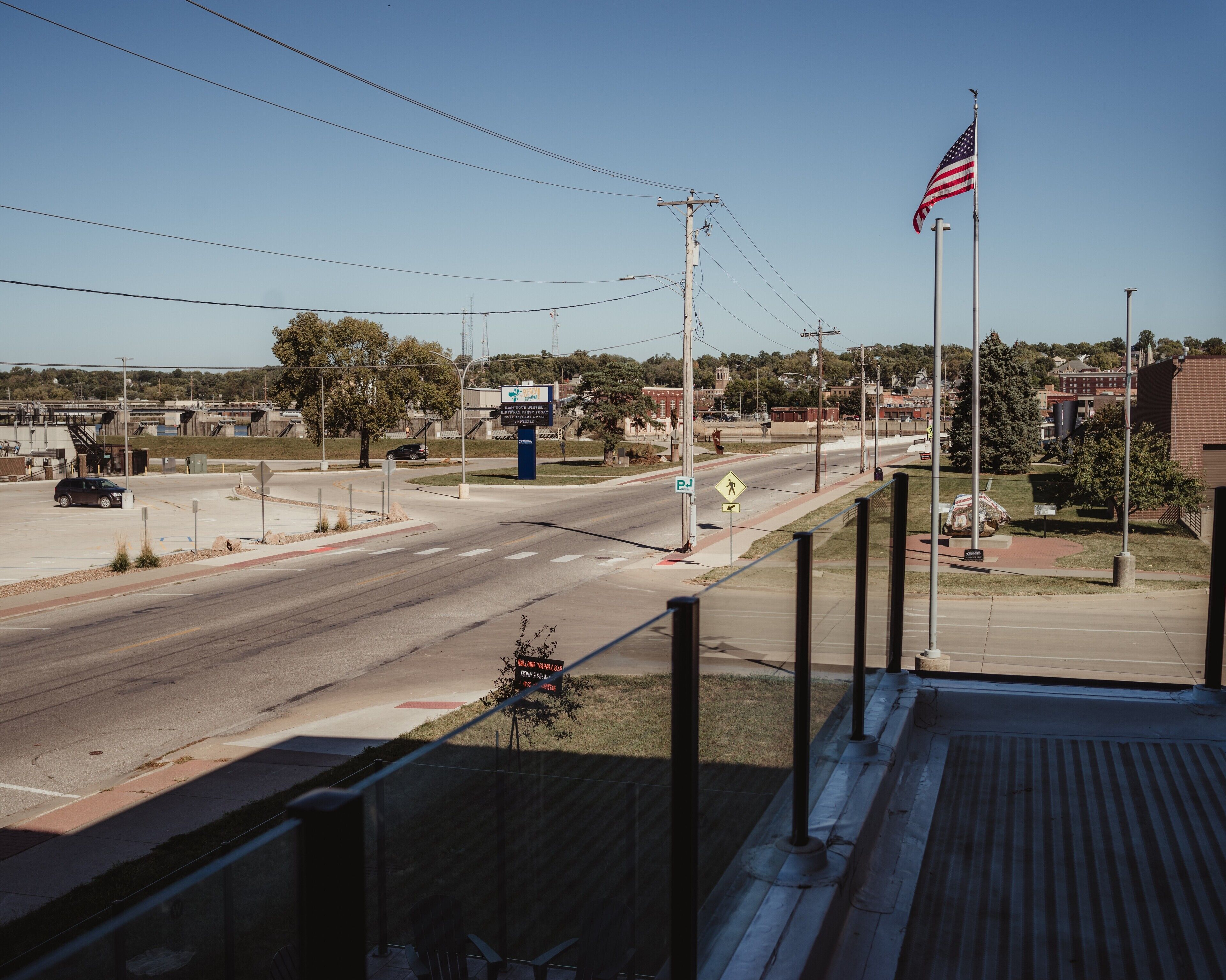 A street view with a pedestrian crossing, a flagpole with an American flag, and a clear sky.