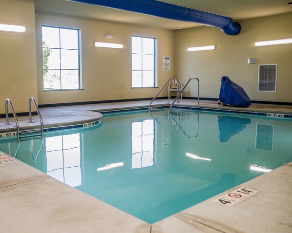 An indoor swimming pool with clear water, metal ladders, and a tiled edge.