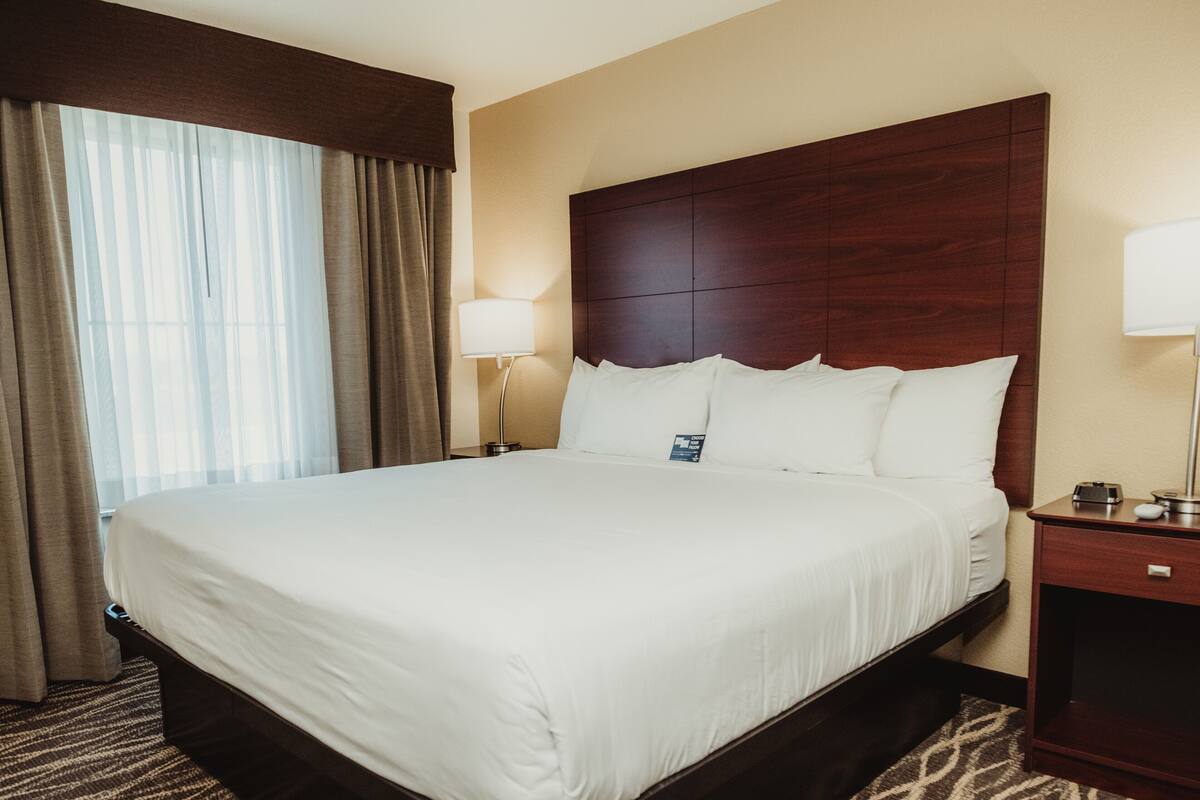 Een hotelkamer met een groot bed, een houten hoofdeinde, een nachtkastje met een lamp en een kamerbreed tapijt met dessin.