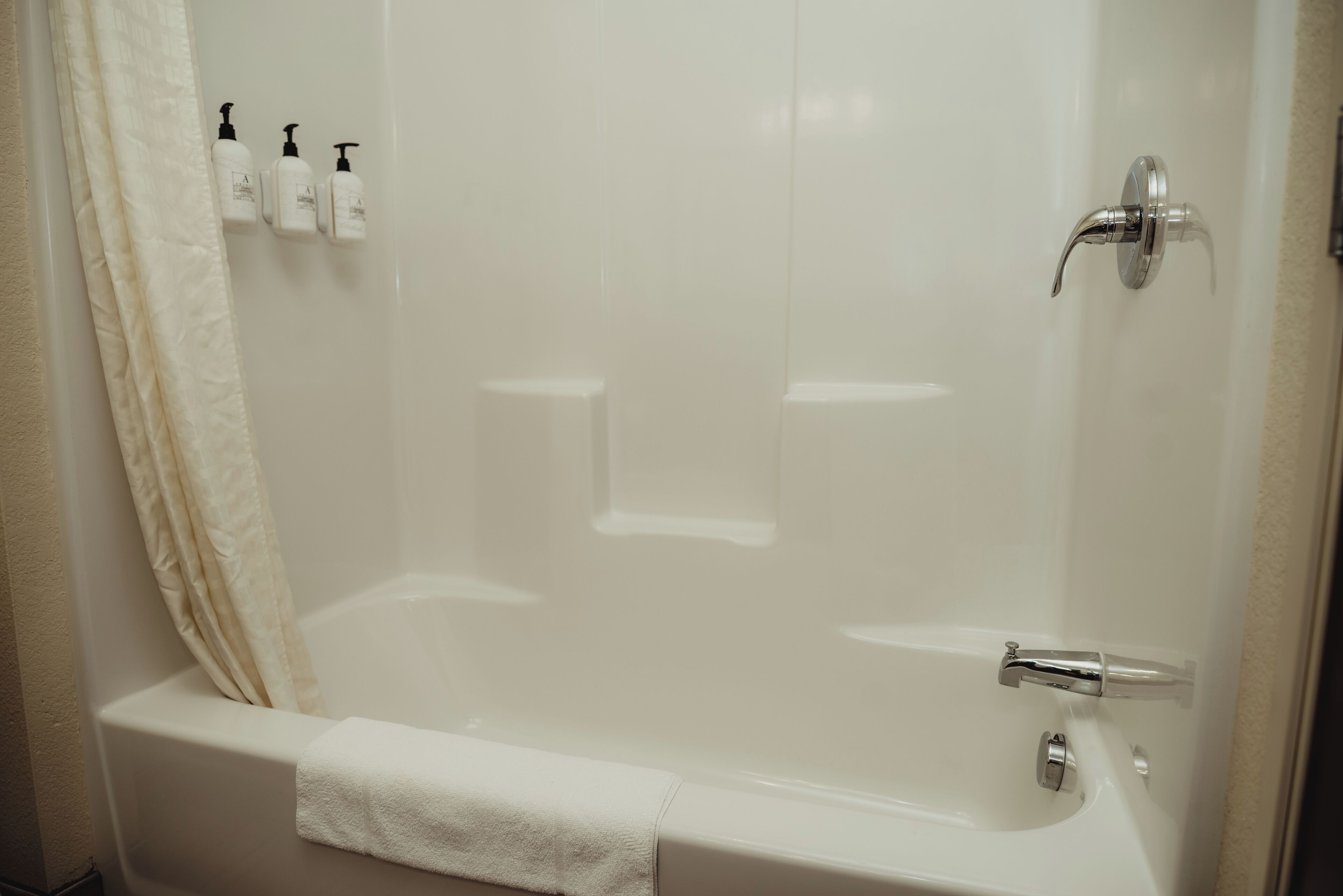 A modern bathroom with a bathtub, a shower, and three bottles of shampoo on the wall.
