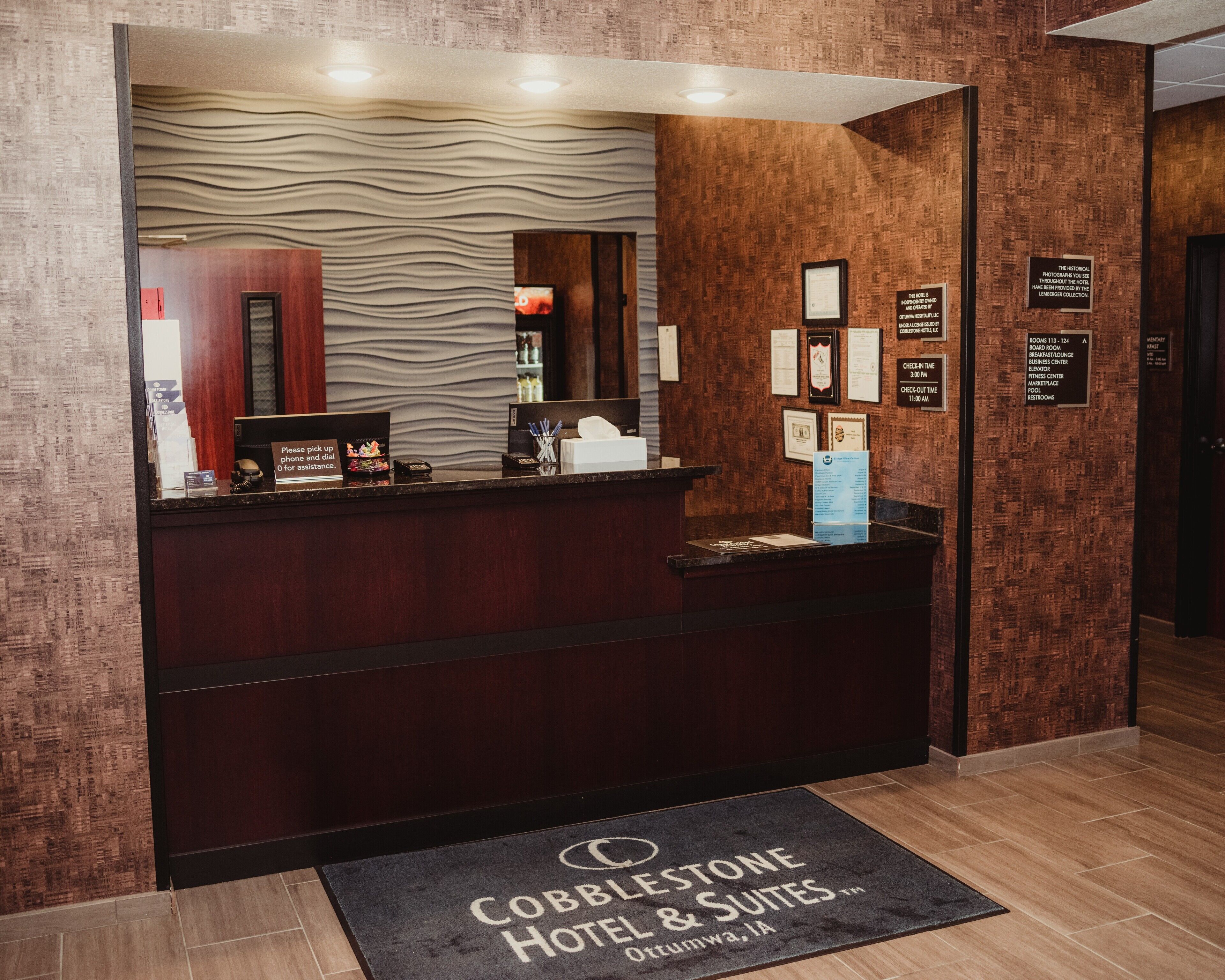A hotel reception desk with a check-in counter, a digital screen, and a wall-mounted information board.
