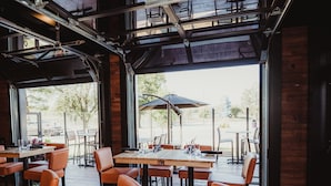 An indoor dining area with tables and chairs, large windows, and an outdoor view.