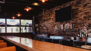 A bar with a long counter, orange chairs, a brick wall, and a mounted TV.