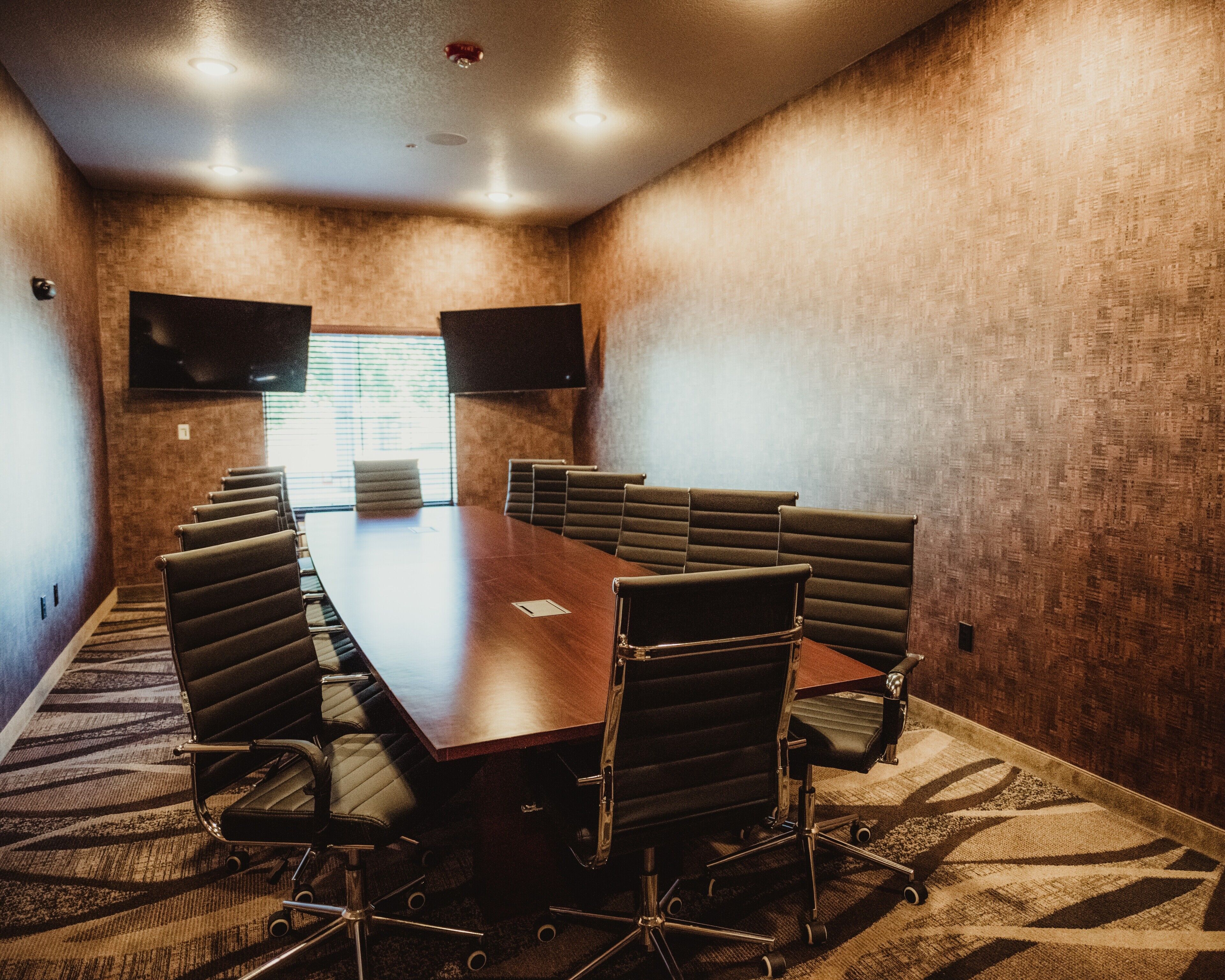 A conference room with a long table, multiple chairs, a flat-screen TV, and a carpeted floor.