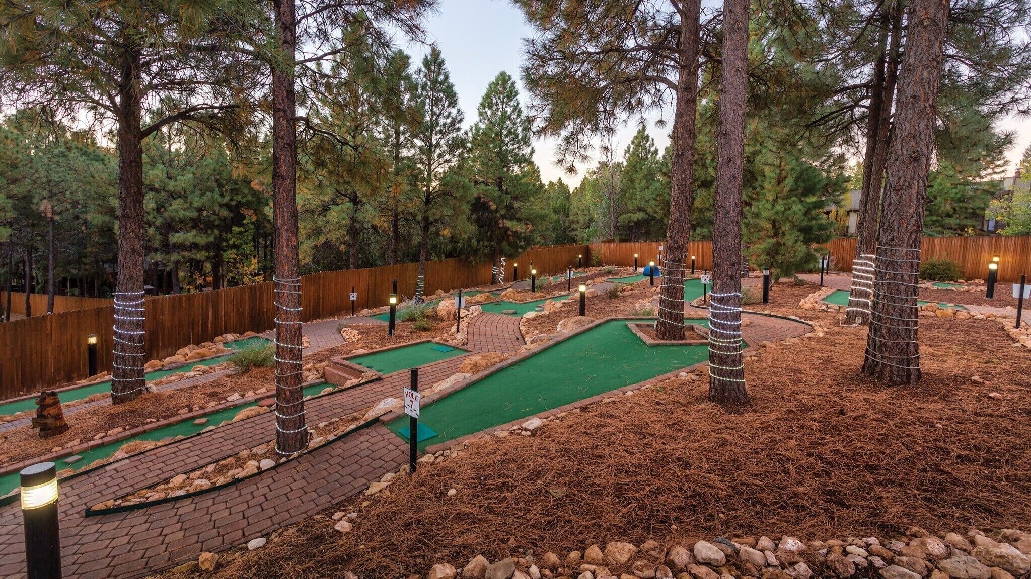 A miniature golf course with green putting greens, brick pathways, and pine trees.