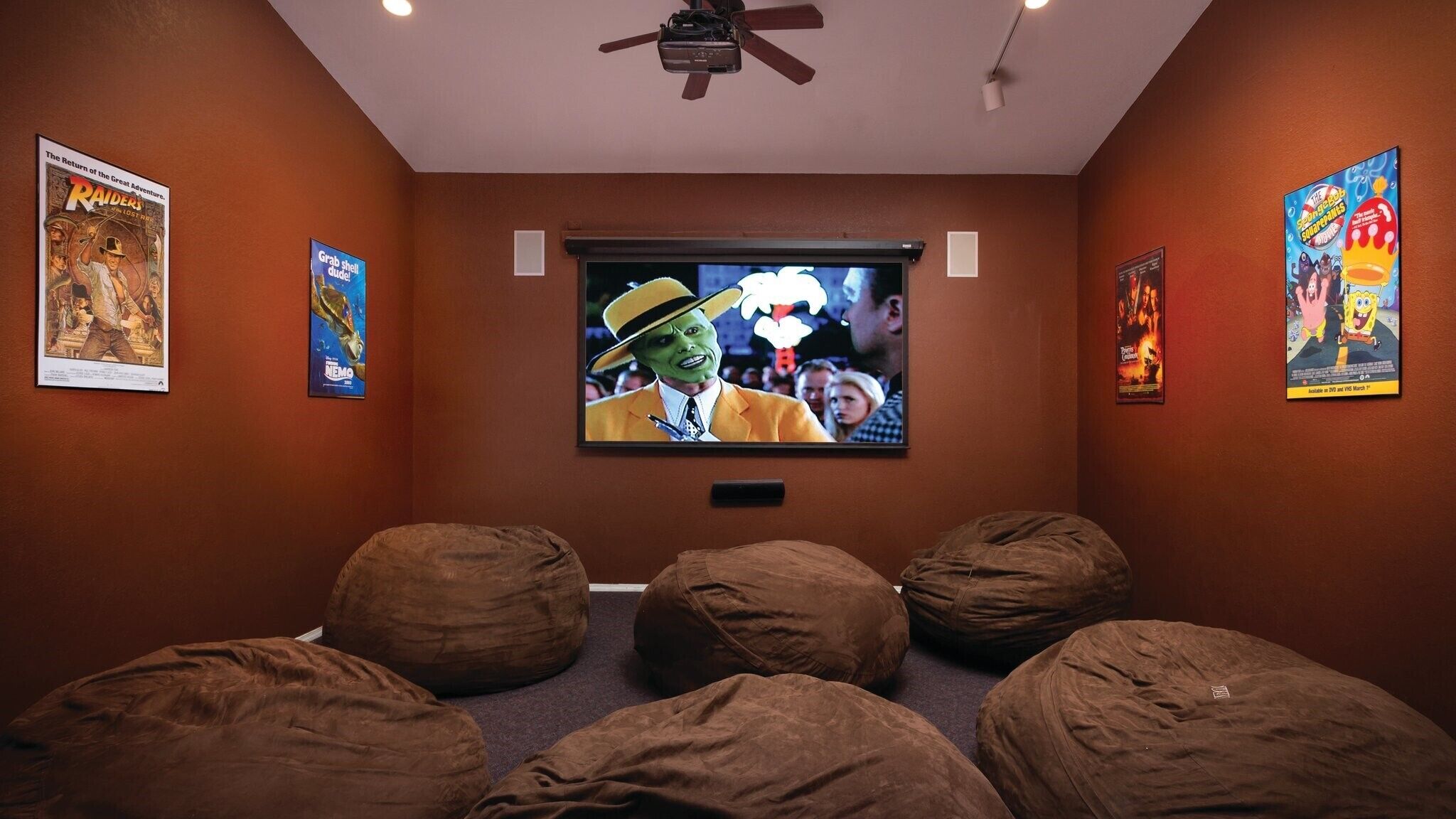 A home theater room with a flat-screen TV, bean bag chairs, and movie posters on the walls.