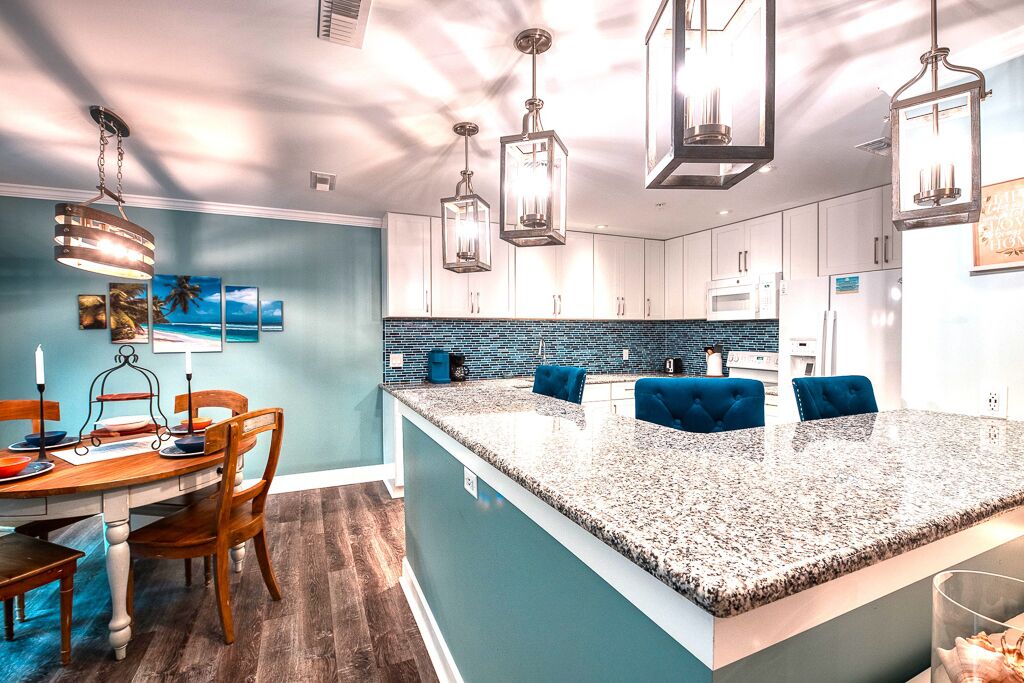 A modern kitchen with a large island, pendant lighting, and a blue accent wall.