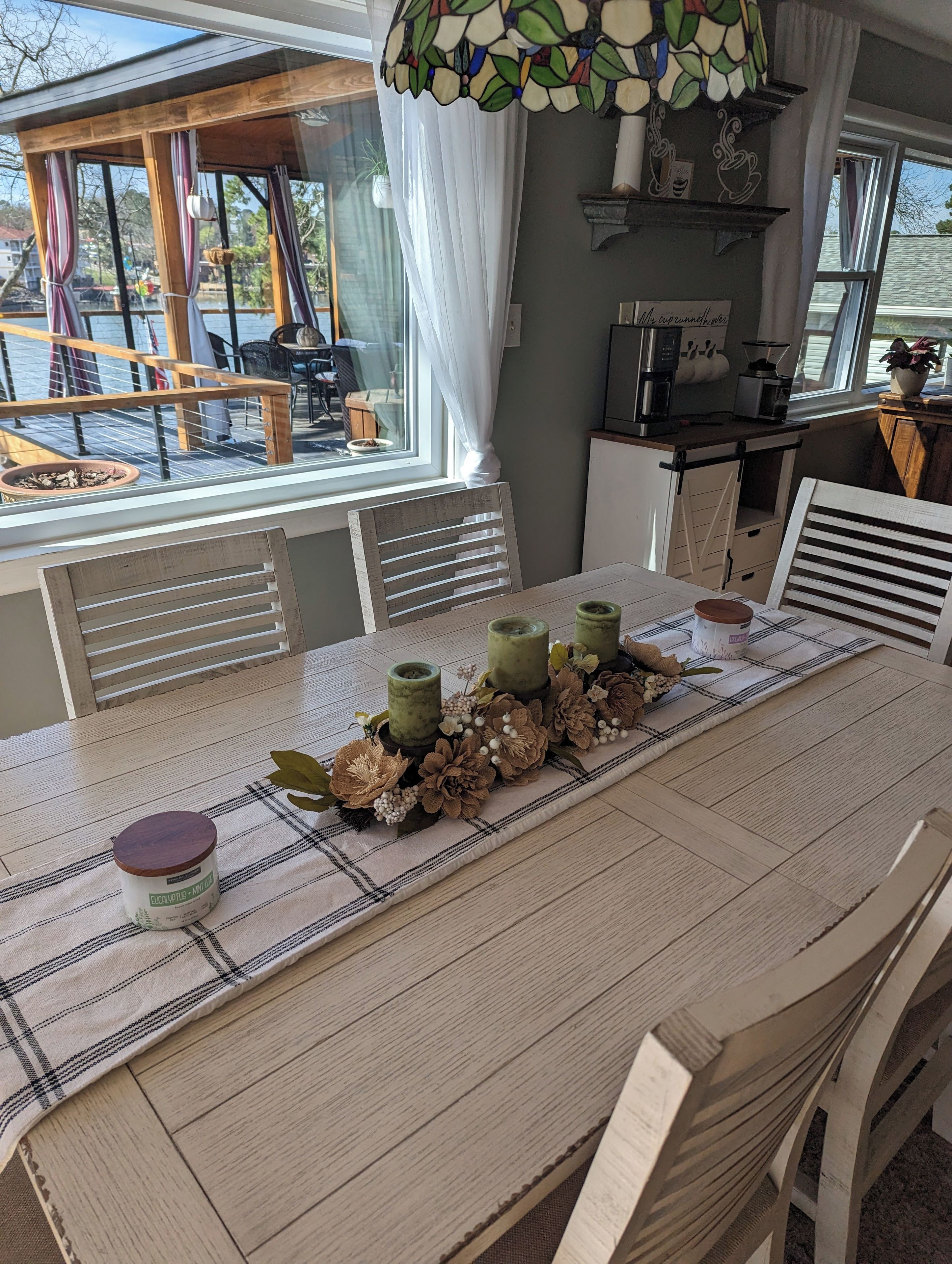 Un'area pranzo con tavolo apparecchiato per quattro persone, caratterizzata da una tovaglia a quadri, tre portacandele verdi e un centrotavola decorativo.