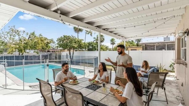 Ett takförsett utomhusområde med plats för måltider, en pool, bord och stolar.