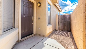 A residential entryway with a dark brown door, a small window with a view of the sky, and a wooden fence. - Your Home away from Home (Goodyear)