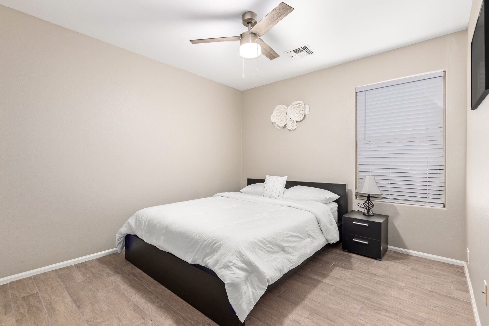 A bedroom with a bed, a nightstand, a lamp, a ceiling fan, and a window with blinds.