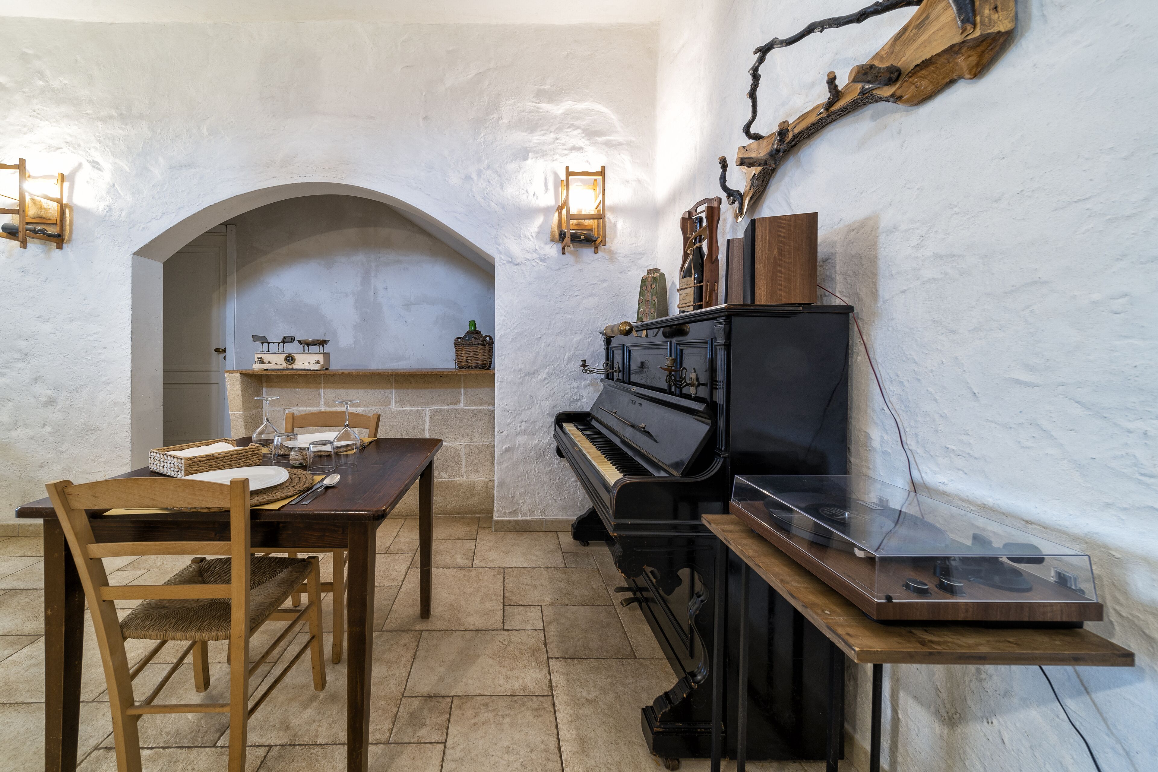 A dining area with a piano, wooden table, chairs, and a stone wall.