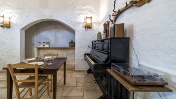 A dining area with a piano, wooden table, chairs, and a stone wall.