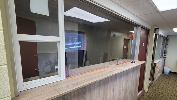 Un comptoir d’accueil avec un plan de travail en bois, une cloison en verre et une vue sur un paysage enneigé par la fenêtre.