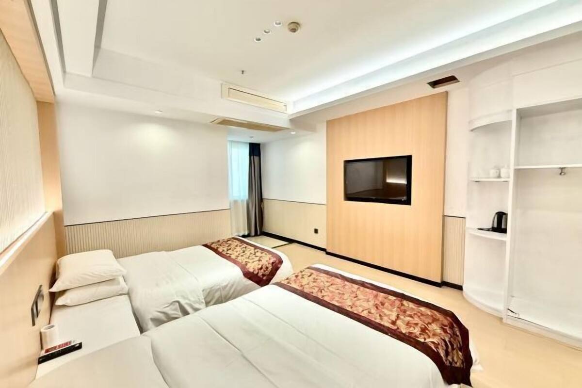 A hotel room with two beds, a TV mounted on the wall, and a wardrobe.