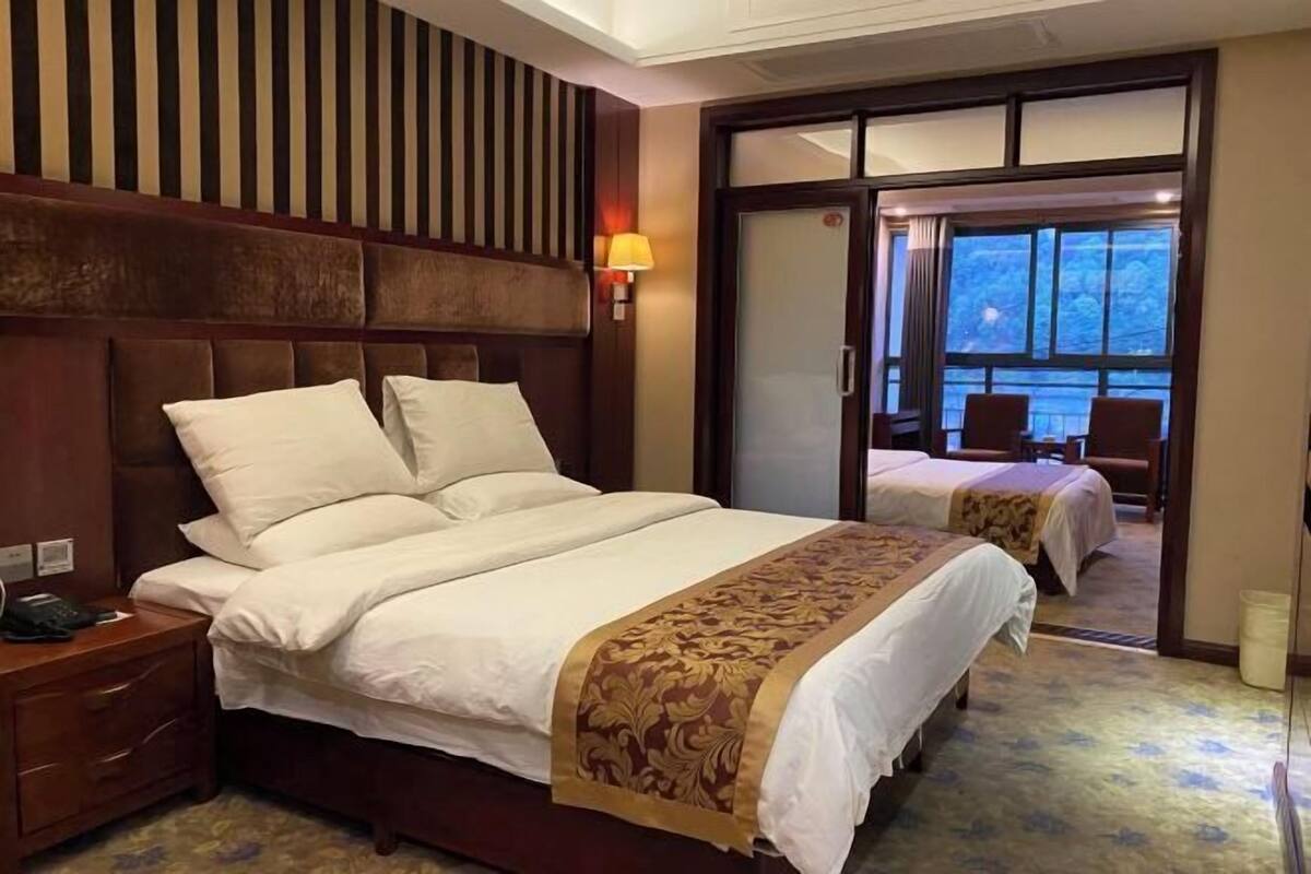 A hotel room with a large bed, a smaller bed, a nightstand, a lamp, and a sliding door leading to a balcony.