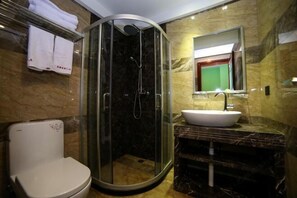 Un baño moderno con ducha de vidrio, inodoro blanco, lavamanos de mármol y espejo sobre el lavamanos.