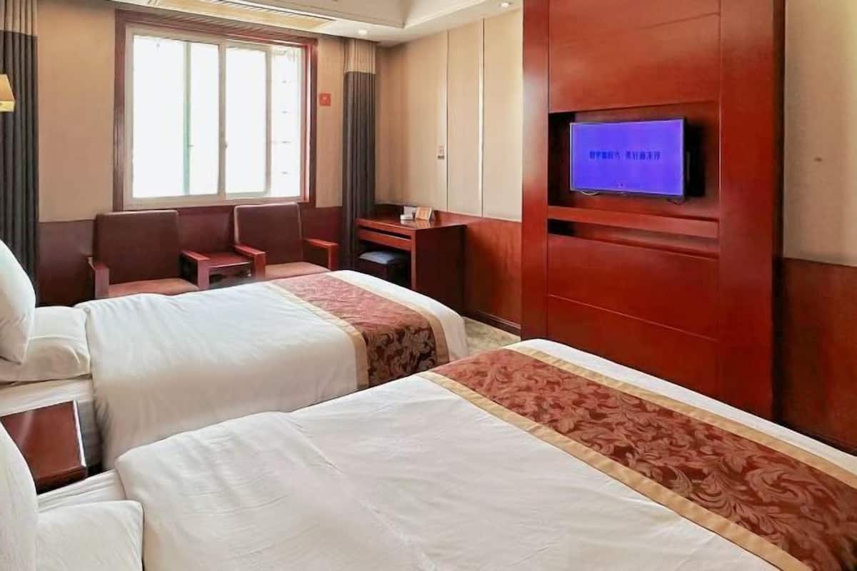 A hotel room with two beds, a TV, a desk, and a chair.